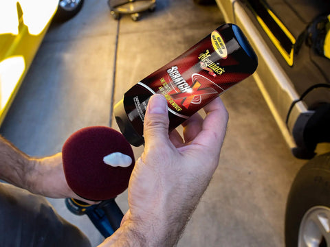 Person holding a bottle of Scratch-X Car Scratch Remover For Fine Scratches And Blemishes Quick Fix Restores Clarity On Glossy Exterior Paint And Clear Coats Ideal For Trucks And SUVs 7 Oz Bottle next to a vehicle.
