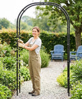 Person assembling a Rustproof Metal Garden Arch Trellis With PE Coating, Easy Assembly, 7.9 Ft High By 4 Ft Wide in a garden setting.