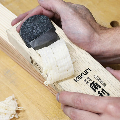 Close up of Pro Grade Japanese Kanna Pull Plane Hitachi Aogami Blue Steel Number Two Blade on wood, showing shavings and oak body.