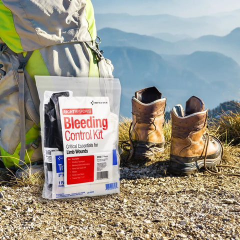 First Aid Only Right Response Bleeding Control Kit for limb wounds, 7 pieces, white pouch, outdoor scene with boots.