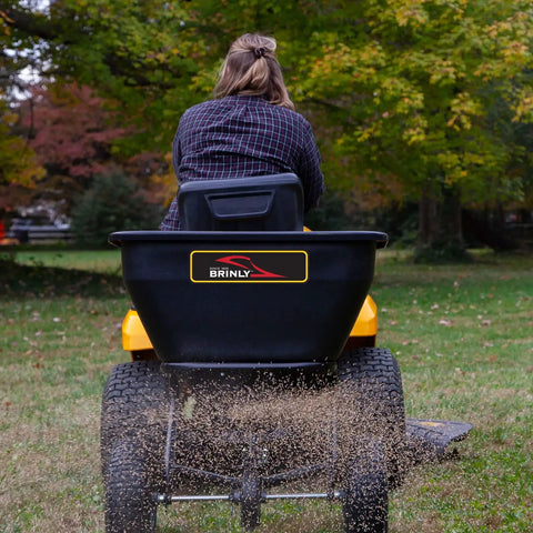 Tow Behind Broadcast Spreader With Universal Hitch 175 Lb Capacity Durable Poly Hopper spreading grass seed on lawn