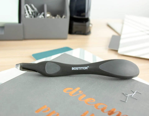 Ergonomic black office staple remover with magnetic pick up, placed on a desk, highlighting its sleek push-style design.