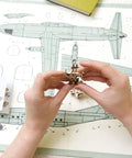 Hands assembling wooden model plane from Four Pack Wooden 3D Aircraft Puzzle Kit For Kids 5 Plus Buildable Mechanical Models.