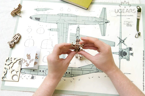 Hands assembling wooden model plane from Four Pack Wooden 3D Aircraft Puzzle Kit For Kids 5 Plus Buildable Mechanical Models.