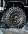 Close-up of Brass Beadlock Wheel Set With Black Coating And S5 1.0 Crawler Tires For Axial SCX24 AX24 TRX4M FCX24 Upgrades 1/24 1/18 RC Crawlers Negative Offset For Wider Stance Durable Bias Ply Build And Aggressive Side Lug installed on RC crawler with rugged tire tread.