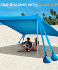 Beach Canopy Sun Shelter 10x10ft With UPF50 UV Protection on sandy beach, two people sitting underneath, blue shelter with poles and sandbags.