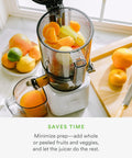Nama J2 Cold Press Juicer Hands Free White Self Feeding Hopper filled with fruits, clear container visible, placed in kitchen setting.