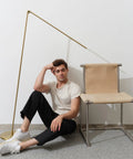 Libra LED Floor Lamp With Adjustable Pivot Arm And Built In Dimmer next to chair with man on floor.