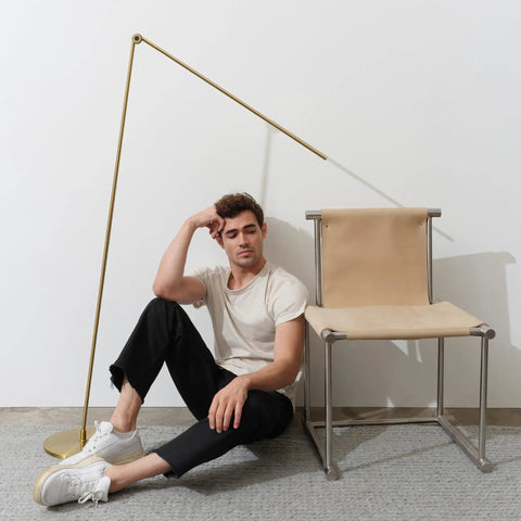 Libra LED Floor Lamp With Adjustable Pivot Arm And Built In Dimmer next to chair with man on floor.