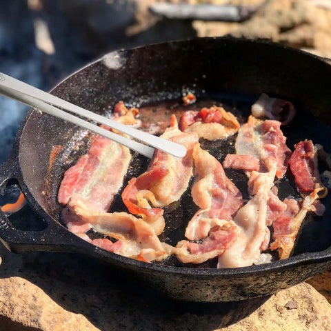 12 Inch Stainless Steel Kitchen Tongs And Tweezers 2 Piece Set in use flipping bacon in a skillet over open flame