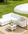 Outdoor patio with white sofa, coffee table, and umbrella on wooden deck.
