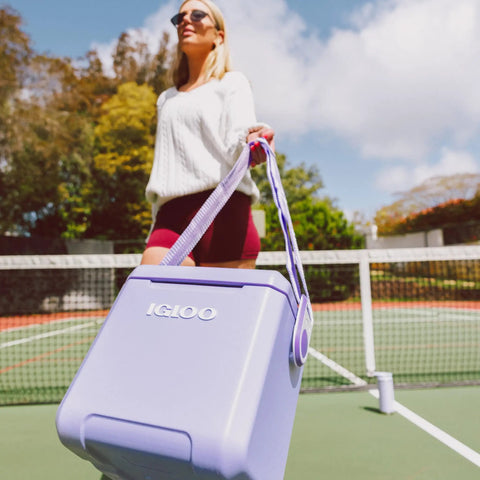 Woman carrying Lilac Breeze 11 Qt Tag-Along Cooler With Strapped Crossbody Carry, Leakproof Lid Locks, MaxCold Insulation on tennis court.