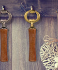 Two wooden-handle bottle openers with gunmetal and brass heads hanging on a rustic wood wall.
