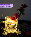 Six Pack Battery Operated Fairy Lights With Timer And Remote Six Point Five Foot Copper Wire 20LED Warm White Twinkle Lights Waterproof Firefly String showcasing waterproof feature in glass
