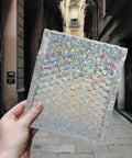 Silver Bubble Envelope Mailers 15x13cm Pack of 20 Self Seal Padded Shipping Bags held in hand, sparkling in sunlight.