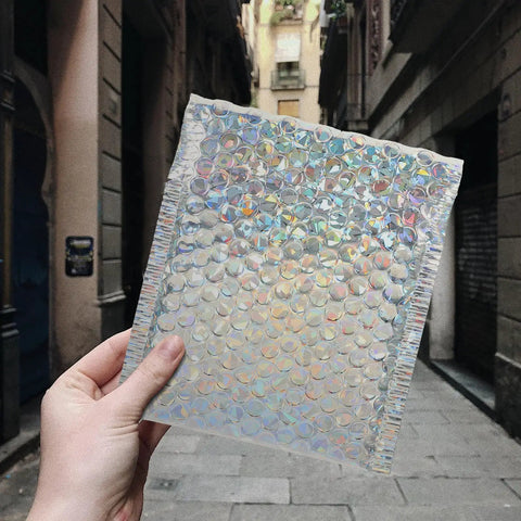 Silver Bubble Envelope Mailers 15x13cm Pack of 20 Self Seal Padded Shipping Bags held in hand, sparkling in sunlight.