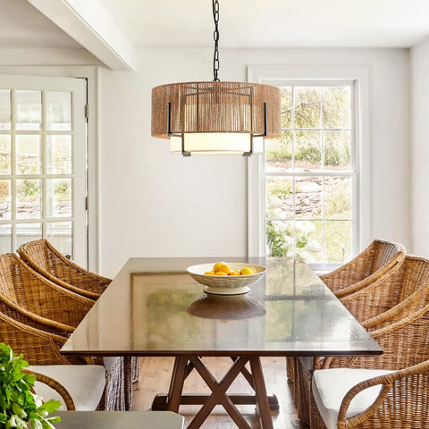 A Straight Up Game Changer 4Light Rattan Chandelier With Linen Drum Shades hanging over a wooden dining table with wicker chairs.