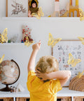 Child in room with Gold Butterflies Wall Decor Kit With 72 Removable Wall Stickers In 3 Styles And 3 Sizes For Party Birthday Wedding Cake Decor And Room Makeover Easy To Apply Kid Approved on wall