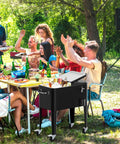 60 Quart Rolling Patio Cooler Cart With Bottle Opener Cap Catcher And Drain beside outdoor dining table at party