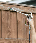 Hand using 12 Inch HEA Extension for High Efficiency Airless Sprayers to paint wooden fence, adds one foot of reach to Control Pro or Titan ControlMax
