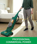 Heavy Duty Bagless Upright Vacuum Chomping Debris On Carpets Hardwood Floors And Furniture With Beastly Suction Plus Onboard Tools And Commercial Filtering For Daily Grind Cleaning in a hotel room.