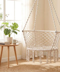 Macrame Hammock Chair With Tassels, Cozy Boho Hanging Swing For Indoor Or Outdoor Use, Beige in a sunlit room by a window.