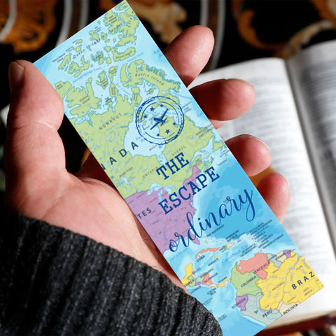 Hand holding a world map bookmark with "Escape the Ordinary" design, part of the World Map Bookmarks Bulk Set 200 Pcs For Reading Goals And Classroom Decor Travel Theme Bookmarks For Teachers And Students Geography Lovers Libraries And Home Reading Inspo set.