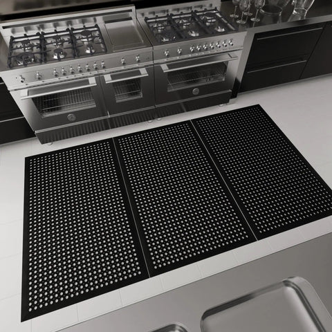 Heavy Duty Rubber Floor Mat With Grippy Non Slip Surface For Commercial Kitchens And Workshops, Waterproof And Hose Washable, Anti Fatigue Comfort, Oil Resistant, Perforated Drainage Design For Indoor Or Outdoor Use, 36 By 60 Inches, Black, installed in a commercial kitchen near stoves.