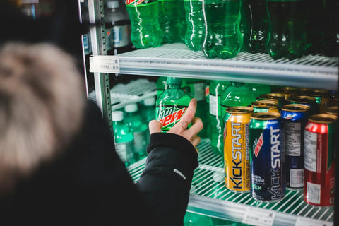 Hand reaching for a bottle of Mountain Dew in a Top Shelf Commercial 3 Door Reach In Refrigerator, Built Tough Stainless Steel Display Cooler Merchandiser For Every Kitchen Grind, Roomy 72 Cubic Foot Layout.