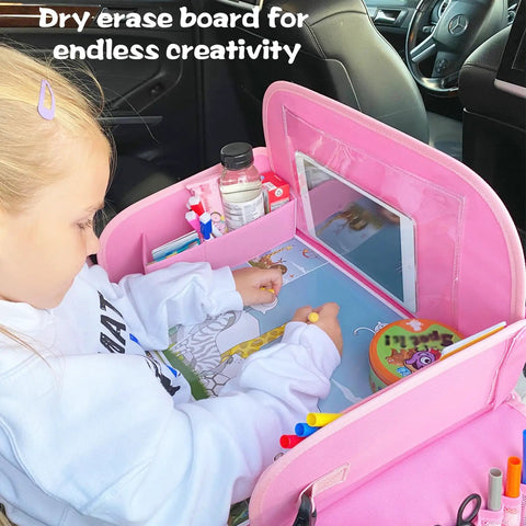 Child using Kids Travel Tray for Car Seat with Ipad Holder and Dry Erase Board Toddler Lap Desk for Road Trips Portable Car Tray with Snack Surface and Activity Tabs Pink in a car.