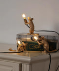 Three Style Resin Mouse Desk Lamp With LED Glow Featuring Running Sitting And Standing Cute Mouse Figures In Gold Finish For Bedroom Or Study Room Decor Plug In Table Light With Easy On Off Switch on a shelf.