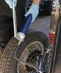 Side view of Lincoln 1147 lever-action grease gun with blue 18-inch whip hose used on a car wheel assembly.