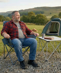 Man sitting on Heavy Duty Portable Camping Chair With 350 Lb Capacity, Extra Wide 1.6 Inch Padded Ergonomic Seat in a campsite.