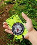 Trail Ready Orienteering Compass Gear For Hiking And Camping Ultra Lightweight Durable Navigation Tool For Backpacking Precise Bearings Green Color Built To Last On Tough Outdoor Adventures, held in hand in forest setting.