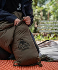Person packing 3-Season Mummy Sleeping Bag For Camping, Hiking, And Backpacking With Water-Repellent Shell into a stuff sack