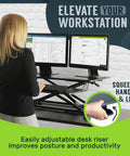 32 Inch Adjustable Standing Desk Converter For Home Office Sit To Stand Desk Setup With Keyboard Tray And Dual Monitor Riser Black Height From 4.3 To 19.7 Inches in use by a person with squeeze handle feature shown