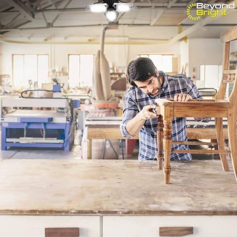Beyond Bright LED Ultra Bright Garage Light With Three Adjustable Panels illuminating a workshop with a woodworker at table
