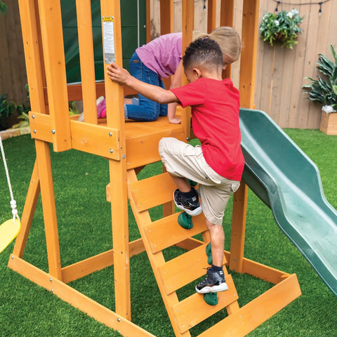 Children climbing a rock wall ladder on a weatherproof wooden swing set for backyard with UV and mold protection, durable pre-treated lumber.