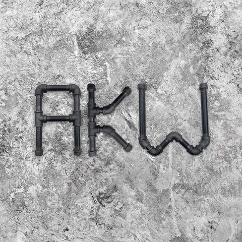Metal pipes arranged to form the letters 'AKW' on a textured stone background.