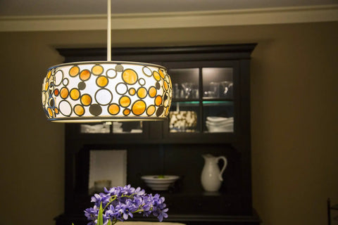Decorative hanging light fixture with circular patterns in dining room set against a dark cabinet background.