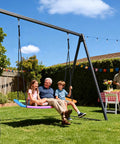 700 Pound Capacity Giant 60 Inch Skycurve Platform Tree Swing For Kids And Adults With Two Hanging Straps Rainbow Patented Design Perfect For Backyards And Outdoor Playgrounds Safer Longer Fun With Easy Assembly. Image shows elderly man with two kids enjoying rainbow swing.