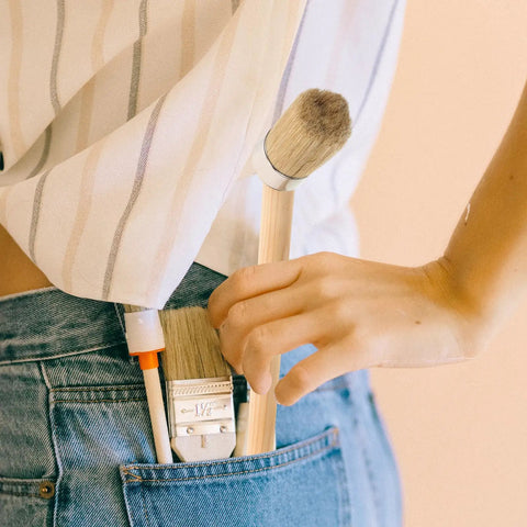 Person holding wood stain and paint brush with wooden handle 50mm round head in jeans pocket, ideal for home projects.