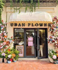 Urban flower shop facade with pink wooden double-sided business hours sign displayed on door with time stickers for small businesses.
