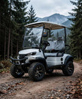 Top Shelf Two Seater Electric Golf Cart With 5kW Motor And 60V Battery Serving 20 Mph Cruising Speed Over 44 Mile Range Rock Solid Suspension And Ample Storage Built Tough For Parks Hotels Or Weekend Warriors In Crisp White parked on a dirt path in a forest.