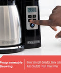 Person adjusting control panel on the 12 Cup Thermal Programmable Coffee Maker with Brew Strength and Vortex Technology, Black and Steel Finish.