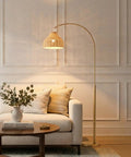 Lark Arc Floor Lamp With Hanging Wicker Shade Brass Tall Standing Light For Living Room And Office Perfect For Reading And Cozy Boho Chic Vibe Decor For Any Space next to a sofa.
