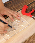 Hand using a pencil on Clear Hardened Acrylic Kickass Star Router Jig Template for precise woodworking cuts.