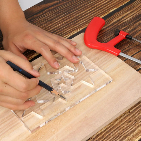 Hand using a pencil on Clear Hardened Acrylic Kickass Star Router Jig Template for precise woodworking cuts.