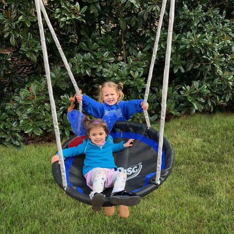 Two children on a round swing, part of a Five-User Four-Station Swing Set With 5 Foot Wave Slide for kids in a backyard setting.