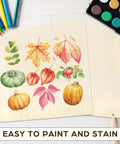 Two light basswood sheets with autumn leaf and pumpkin print; colored pencils and watercolor palette nearby